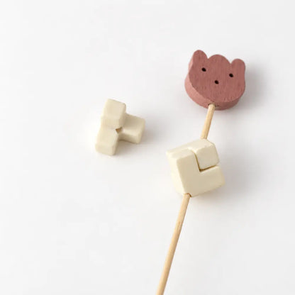 Cream acrylic puzzle bead piece beside two matching pieces assembled into a square on a display rod.