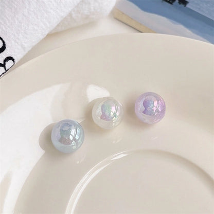 Three blue, white and purple acrylic round beads with an iridescent finish on a white plate in daylight.