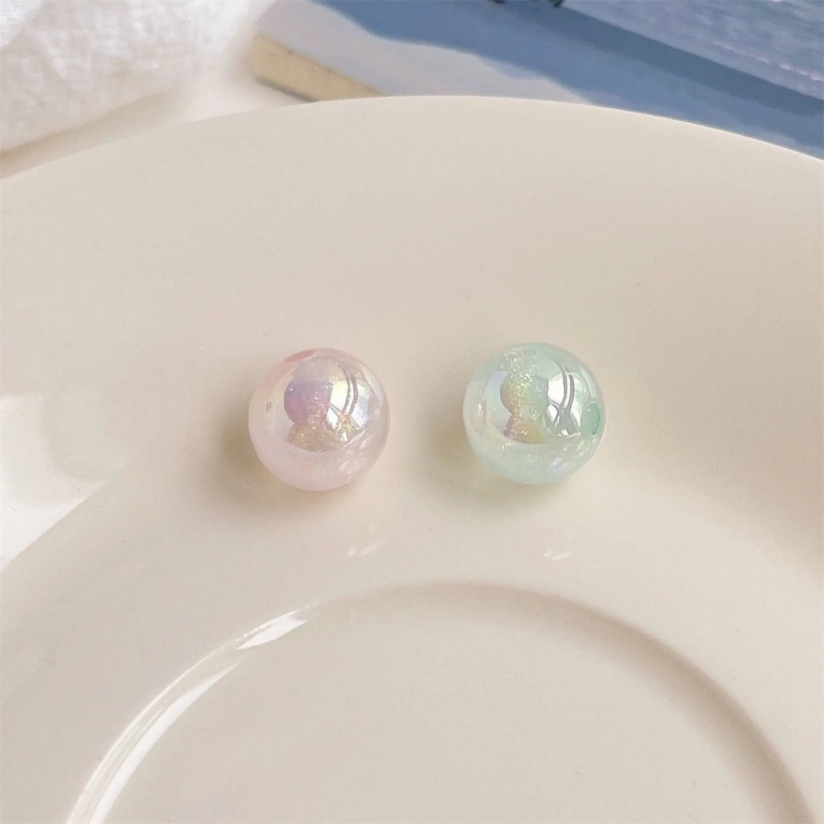 Two pink and green acrylic round beads with an iridescent finish on a white plate in daylight.