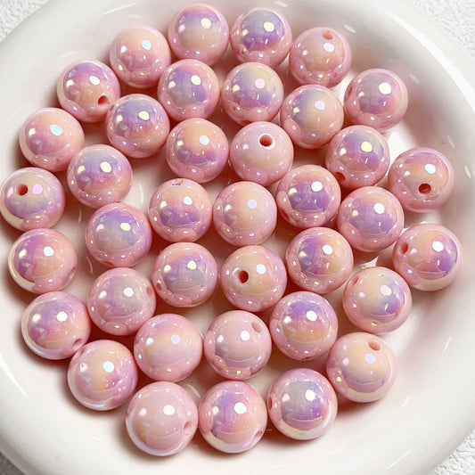 Pink acrylic round beads with a glossy iridescent finish and visible stringing holes on a white plate.