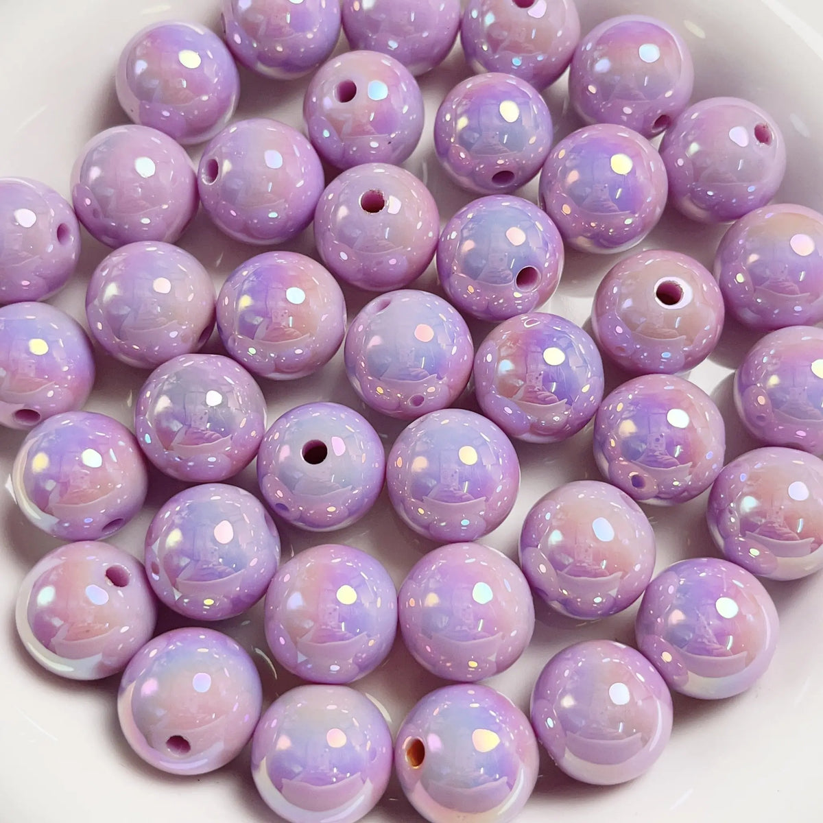 Purple acrylic round beads with a glossy iridescent finish and visible stringing holes on a white plate.