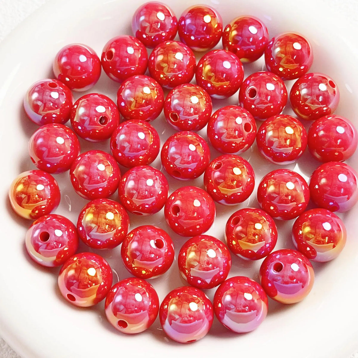 Red acrylic round beads with a glossy iridescent finish and visible stringing holes on a white plate.