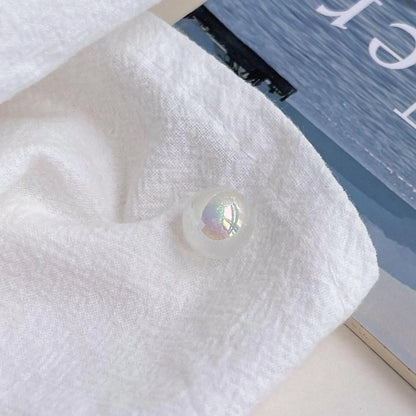 A white acrylic round bead with an iridescent finish shown on textured white cloth in daylight.