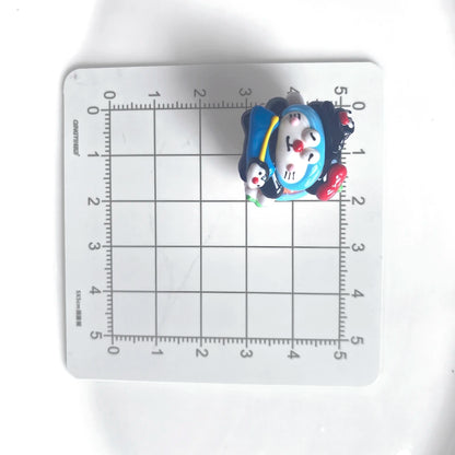 Front view of one blue cat-face bead with a dark hat on a centimeter grid for approximate size reference.