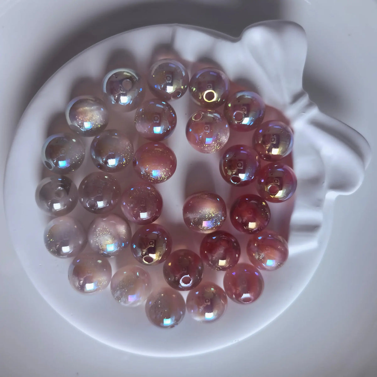 Smoky gray iridescent acrylic round beads with glossy reflections and fine shimmer in a white bow-shaped dish.