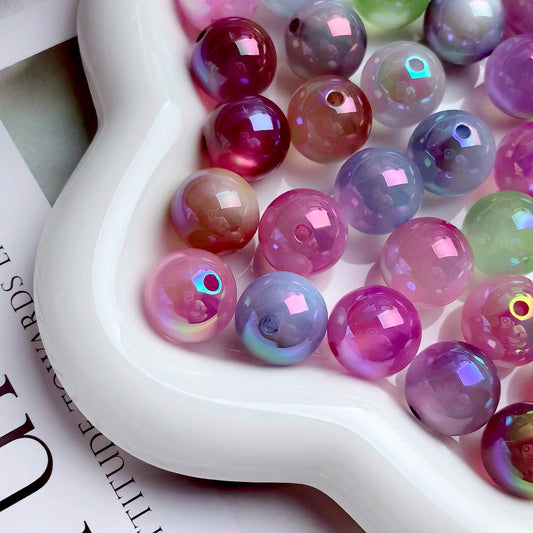 Mixed-color iridescent acrylic round beads in a white dish, showing smooth glossy surfaces and holes.