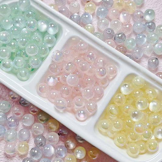 Mixed-color jelly cat-eye acrylic round beads in a divided white tray on pink fabric.
