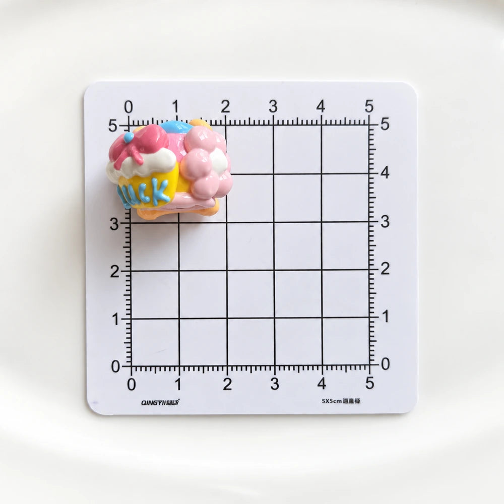 Side view of one hand-painted bead with raised pink and blue details on a centimeter grid for size reference.
