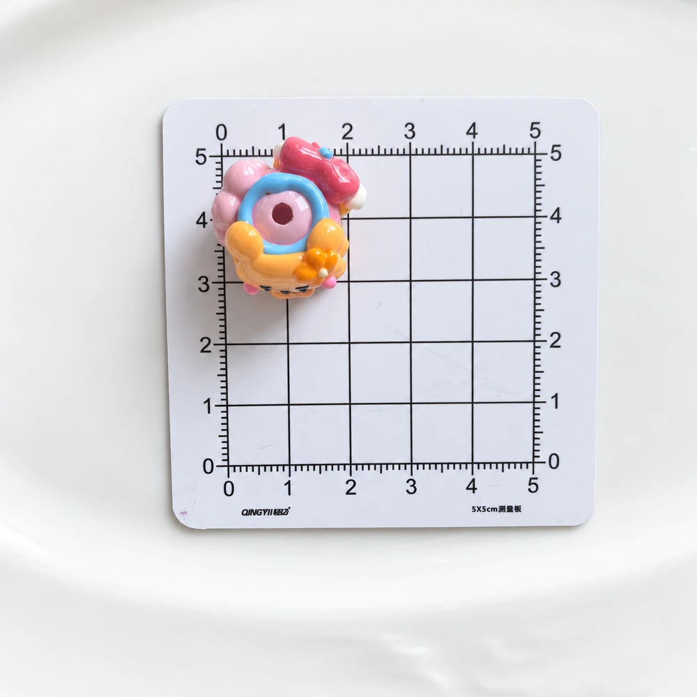 Top view of one decorated acrylic bead showing the threading hole on a centimeter grid for size reference.