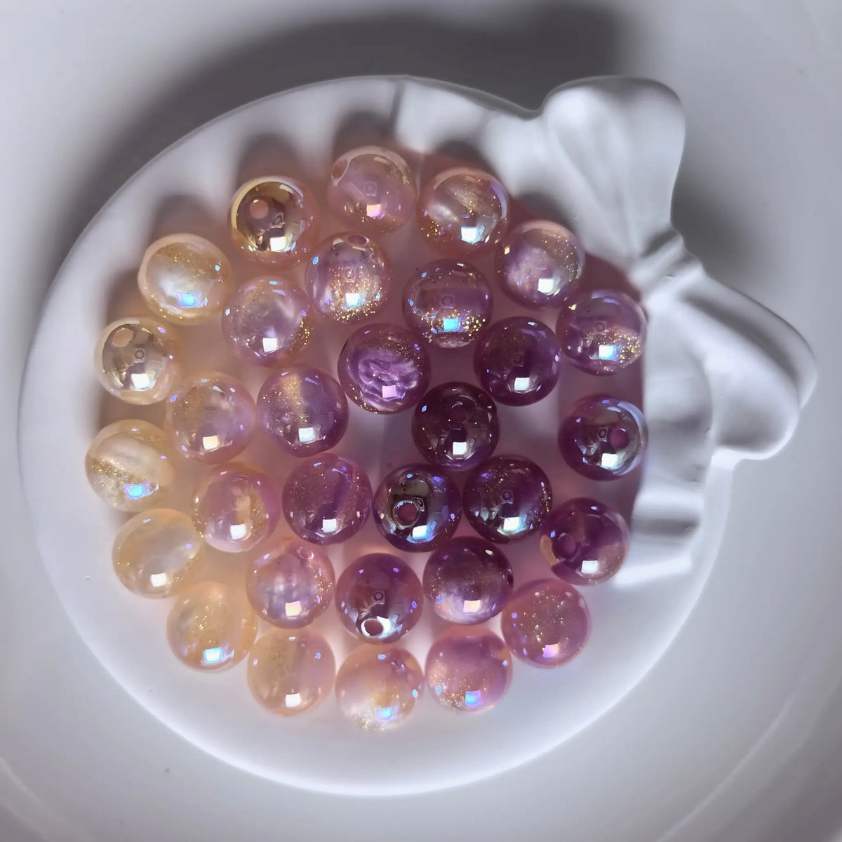 Orange iridescent acrylic round beads with glossy reflections and fine shimmer in a white bow-shaped dish.