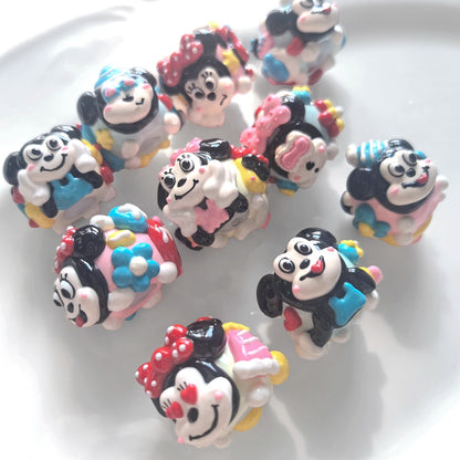 Angled view of a pink and blue hand-painted acrylic bead set showing raised faces, bows and glossy details.