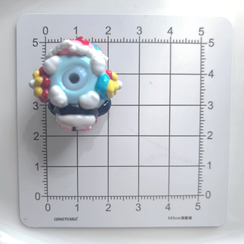 Top view of one decorated acrylic bead showing the threading hole and raised details on a centimeter grid.