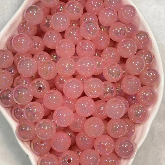 Pink galaxy cat-eye acrylic round beads with fine sparkle and glossy reflections in a white dish.