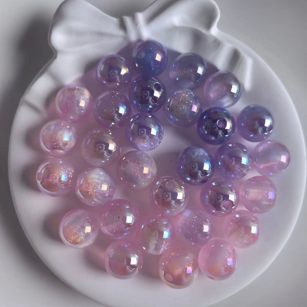 Pale pink iridescent acrylic round beads with glossy reflections and fine shimmer in a white bow-shaped dish.