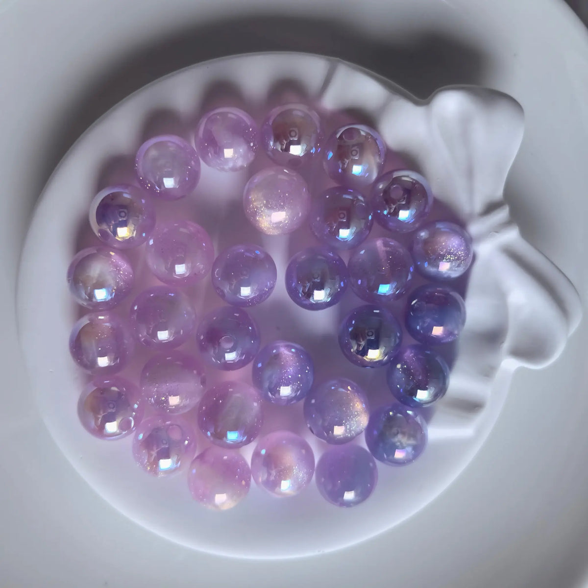 Purple iridescent acrylic round beads with glossy reflections and fine shimmer in a white bow-shaped dish.