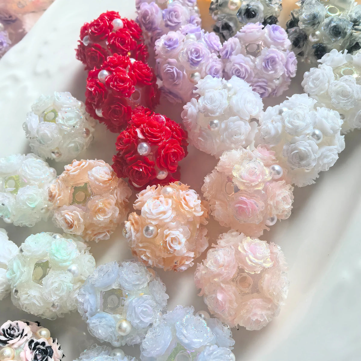 Assorted rose flower ball beads on a white tray, showing layered flowers and pearl-like accents.