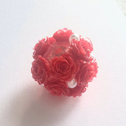 Red rose flower ball bead with raised rose petals, pearl-like accents and a threading hole, shown on white fabric.