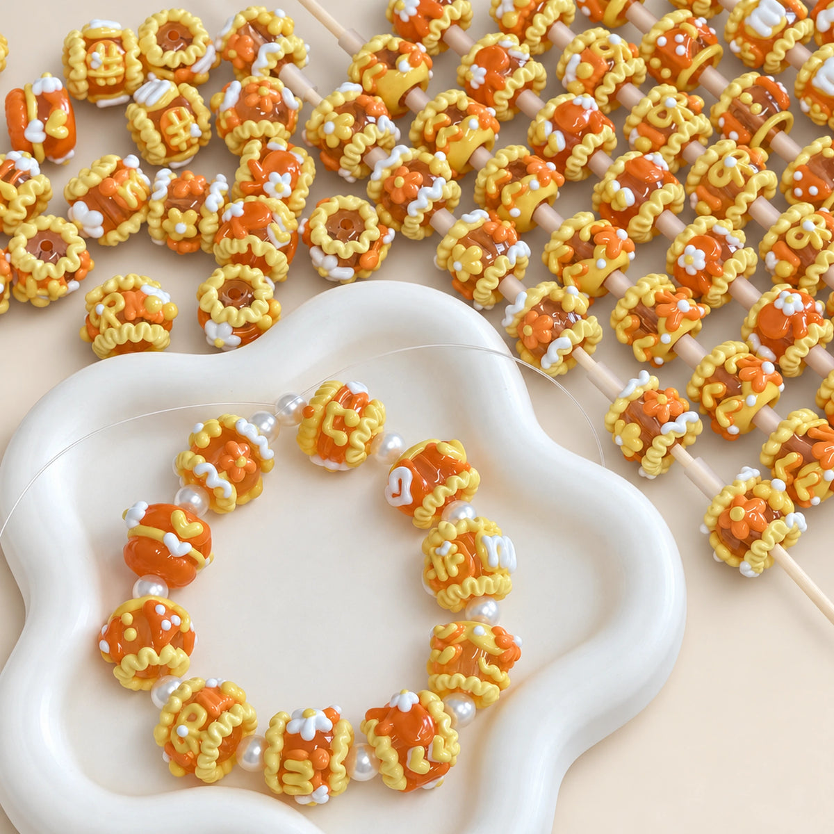 Close-up of translucent orange jelly 3D beads with yellow icing-like swirls and white floral accents threaded on rods