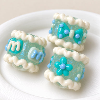 Three handmade luminous mint glitter beads with raised cream ruffles, aqua flower and bow details