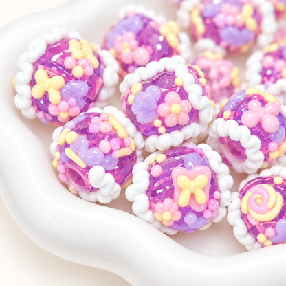 Taro grape purple decorative beads with pastel pink flowers cream borders and glossy 3D motifs, close-up photo